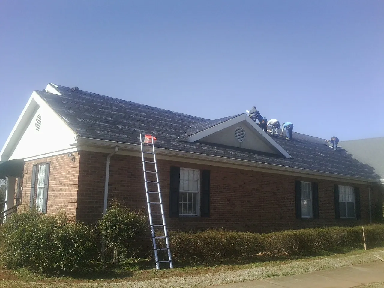 Crew tearing shingles off a brick ranch roof with a ladder set — Metal Roof Repair work by our crew in Cottage Grove